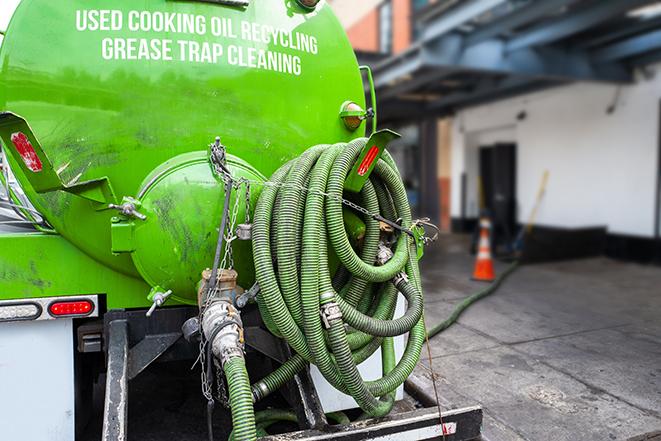 a professional plumber using a pump to empty a grease trap in Addison